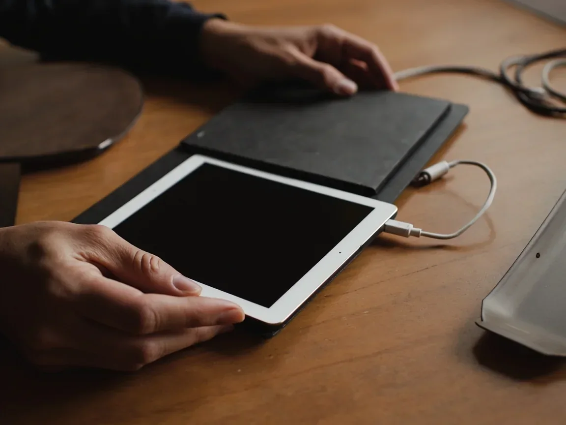 Hands on a closed tablet with a coiled charging cable and a rummy tray aside