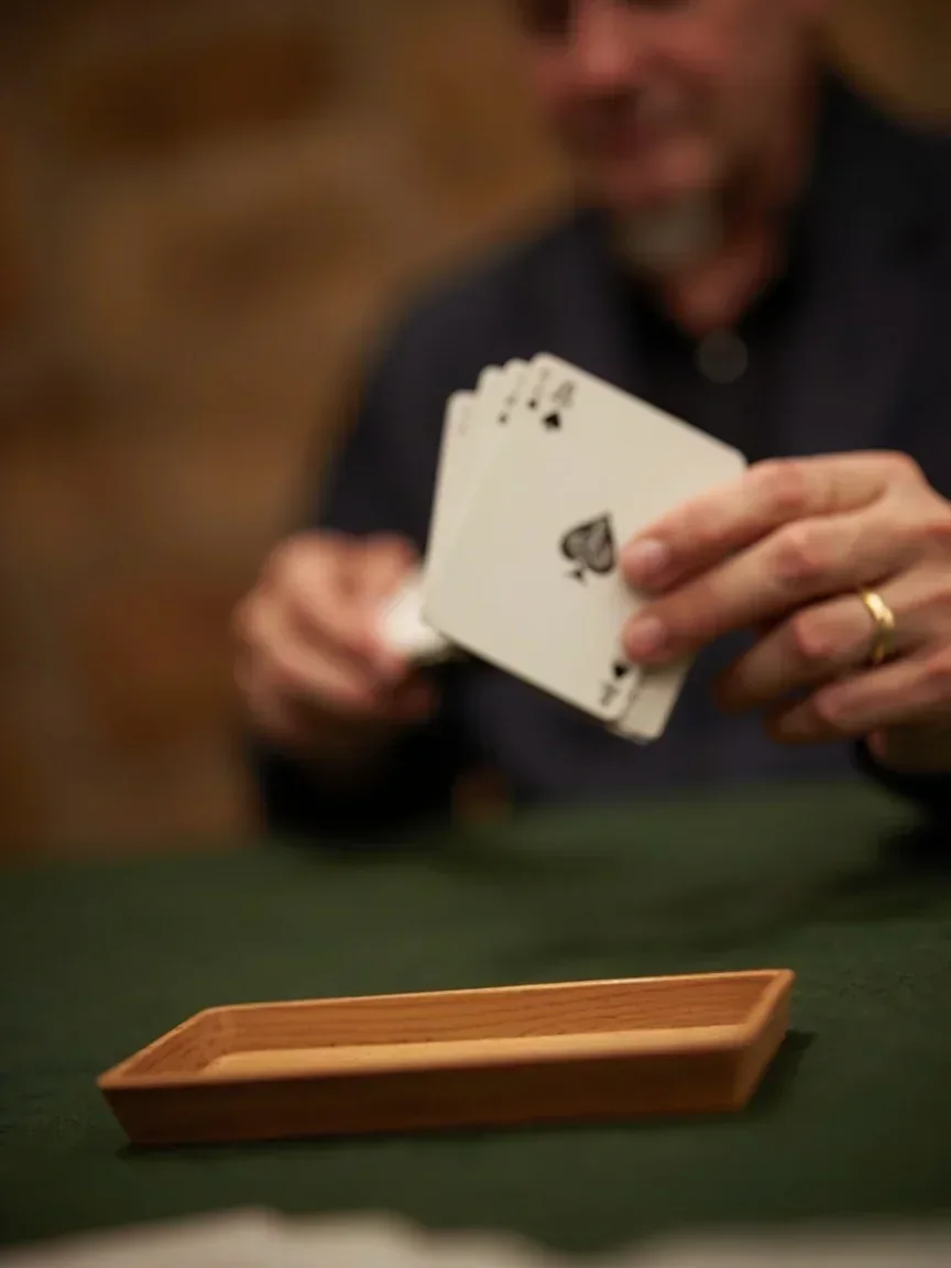 Adult hands holding one card toward a discard tray while the remaining fan stays close
